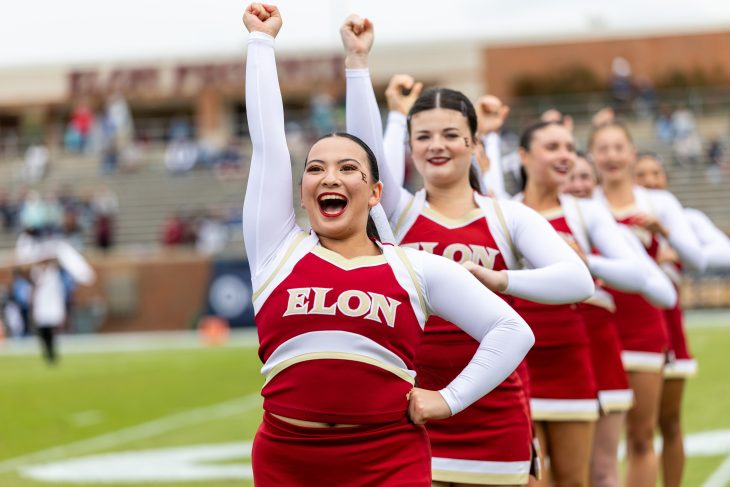 Elon University cheerleaders hold their arm in the air excitedly