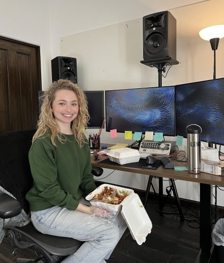 Lillian sits down at her editing desk, eating before preparing to edit a film.
