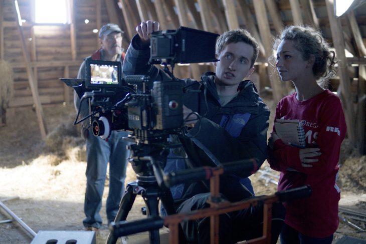 Lillian, pictured holding a notebook while looking into a film camera next to another director.