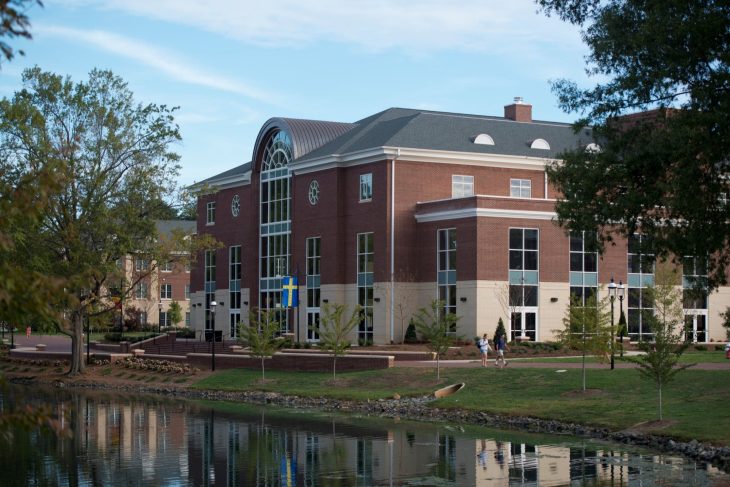Multistory brick building situated near a small lake with a fountain