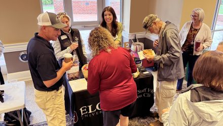 A crowd of people stand in front of a table with a black cloth and talk to multiple members of human resources.