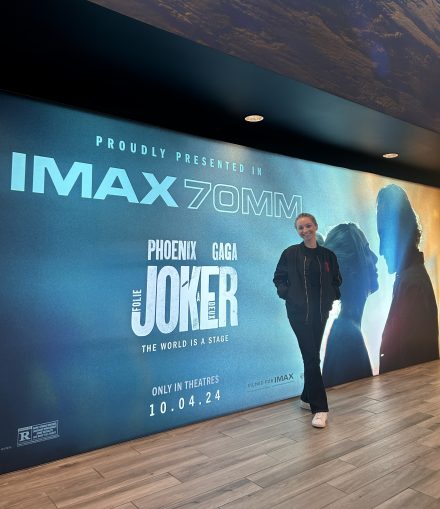 Lillian poses in all black next to a large screen showing the Joker 2 film poster in 2024.