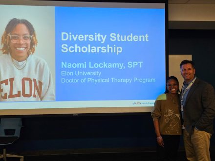 Two people pose for a photo next to a presentation screen that reads "Diversity Student Scholarship Naommi Lockamy, SPT Elon University Doctor of Physical Therapy Program"