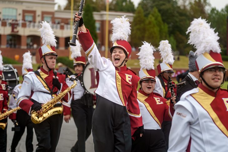 The Elon University "Fire of the Carolinas" marching band walks with one player holding their clarinet in the air