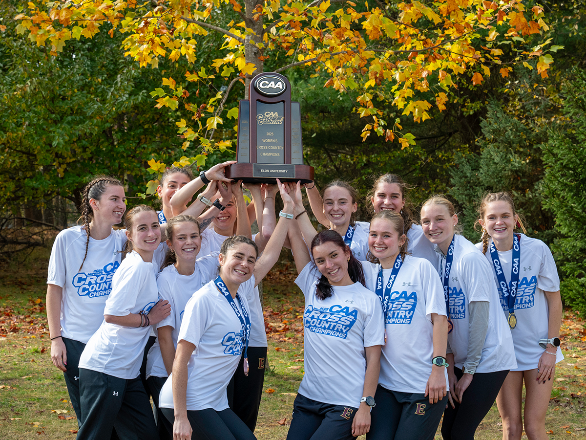 Elon womens cross country team stand in a circle in white shirts and hold up a trophy