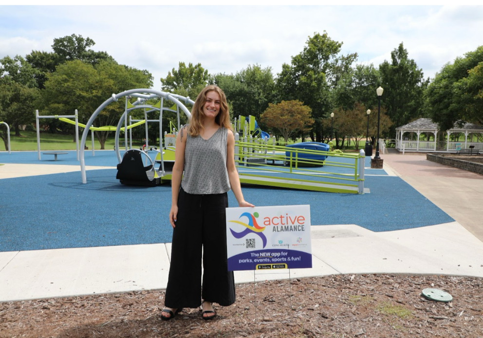 Nicole McGinty '23 stands on a playground next to a yard sign