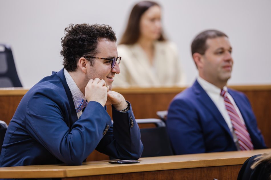 Trey McClenny in a blue suit and tie, smiling, speaking with classmates in an Elon Law classroom.