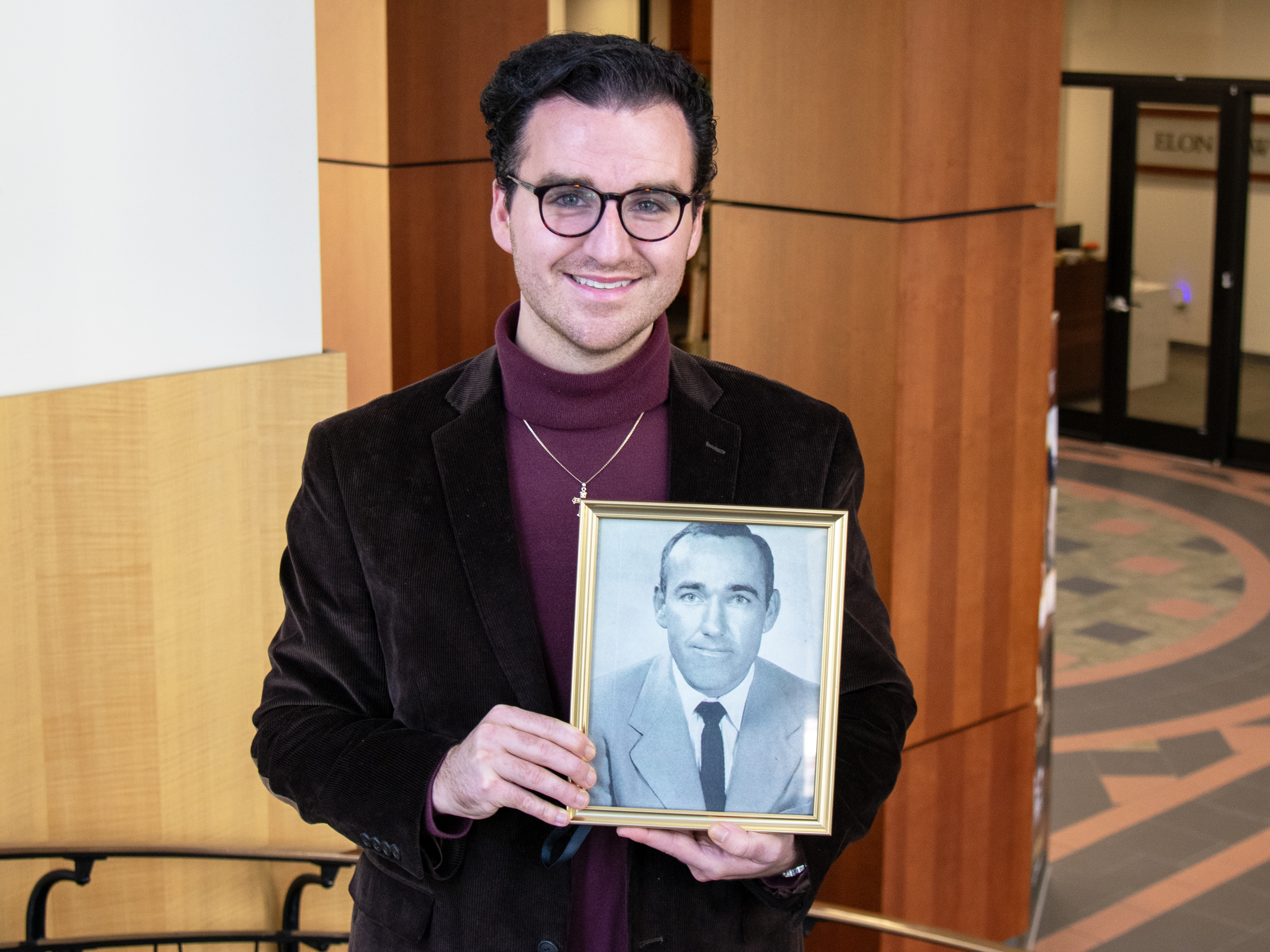Trey McClenny on the steps inside Elon Law holding a framed black and white photo of his grandfather, Dave McClenny