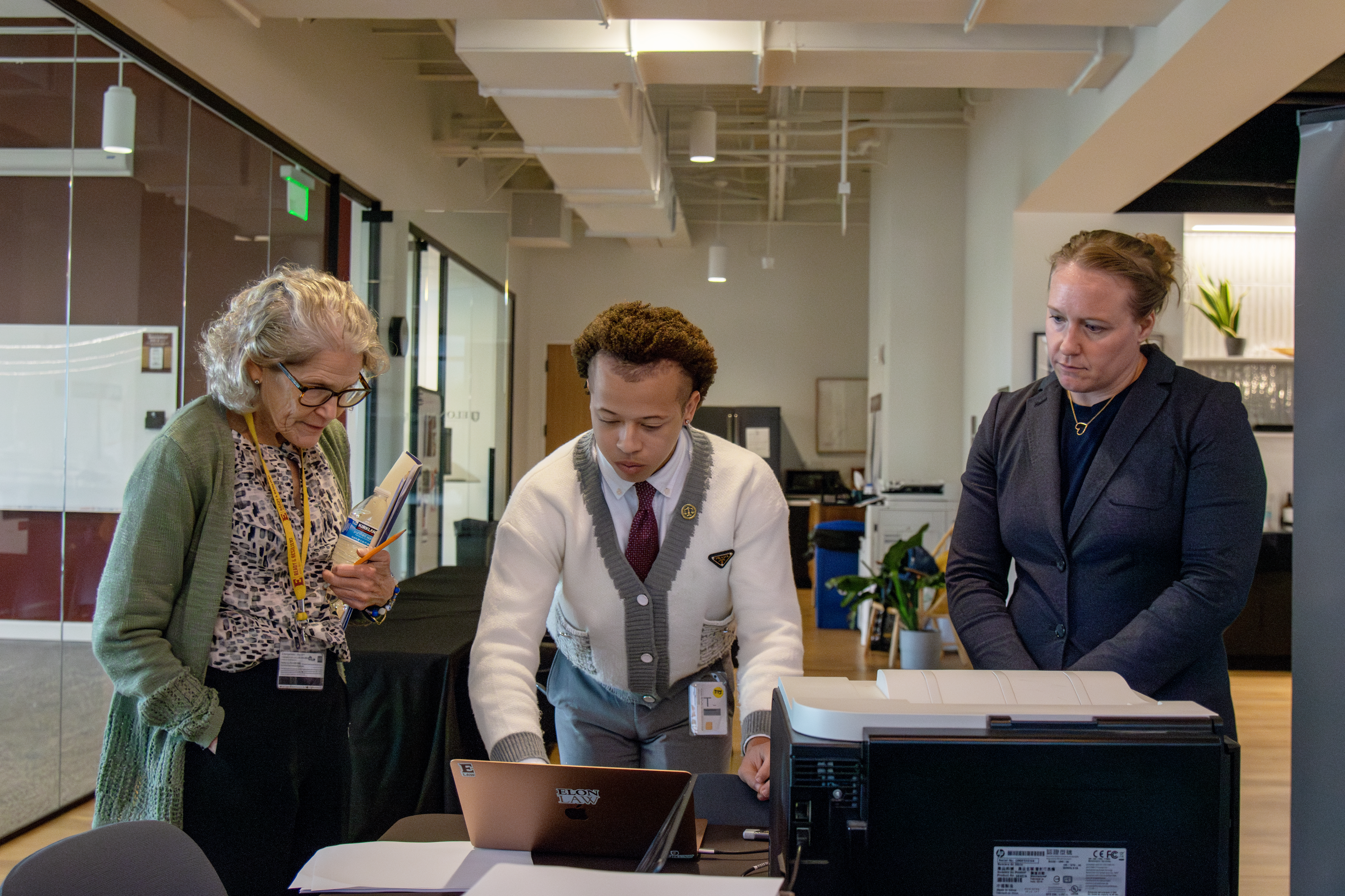 Three people, a man and two women, at a printer reviewing documents