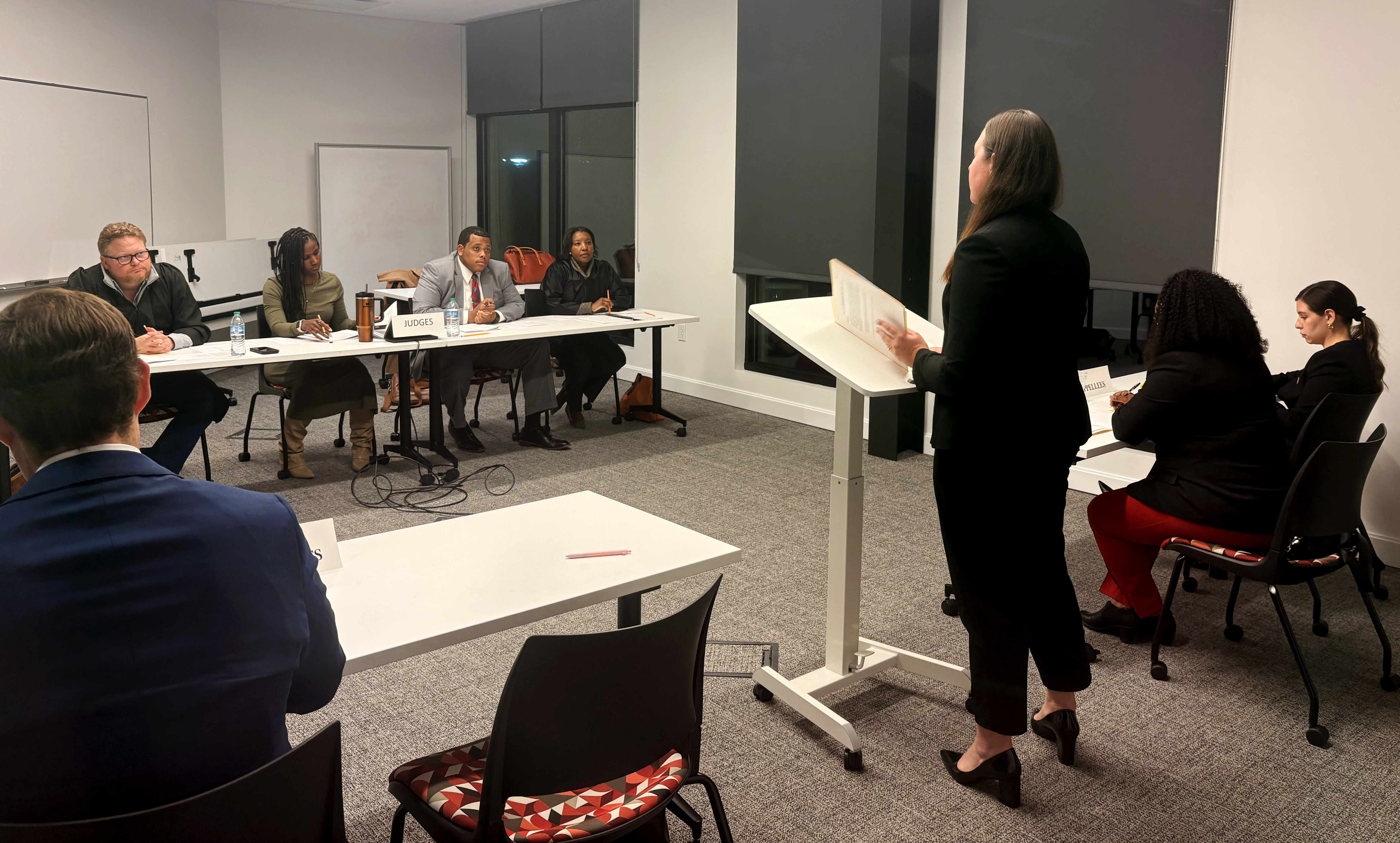 A woman show from behind, speaking at a podium.