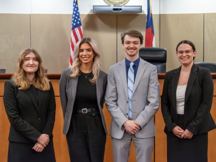 Four students in professional dress in the Robert E. Long Courtroom at Elon Law