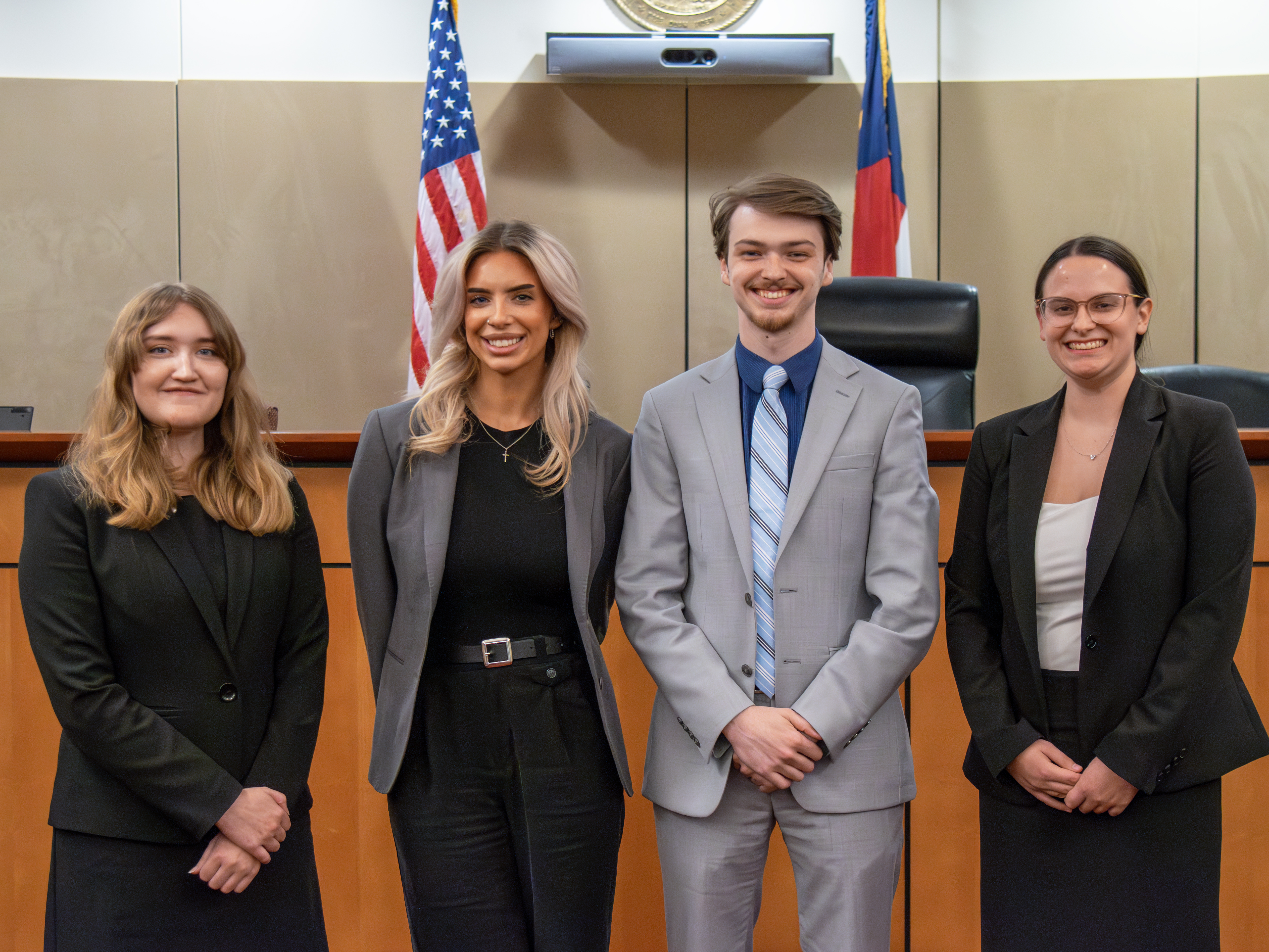 Four students in professional dress in the Robert E. Long Courtroom at Elon Law