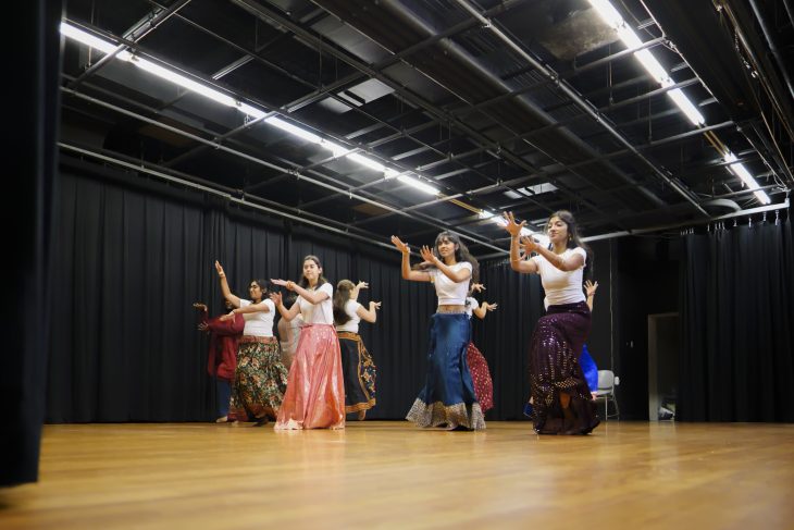 A group of people do a synchronized dance in a room with wooden floors