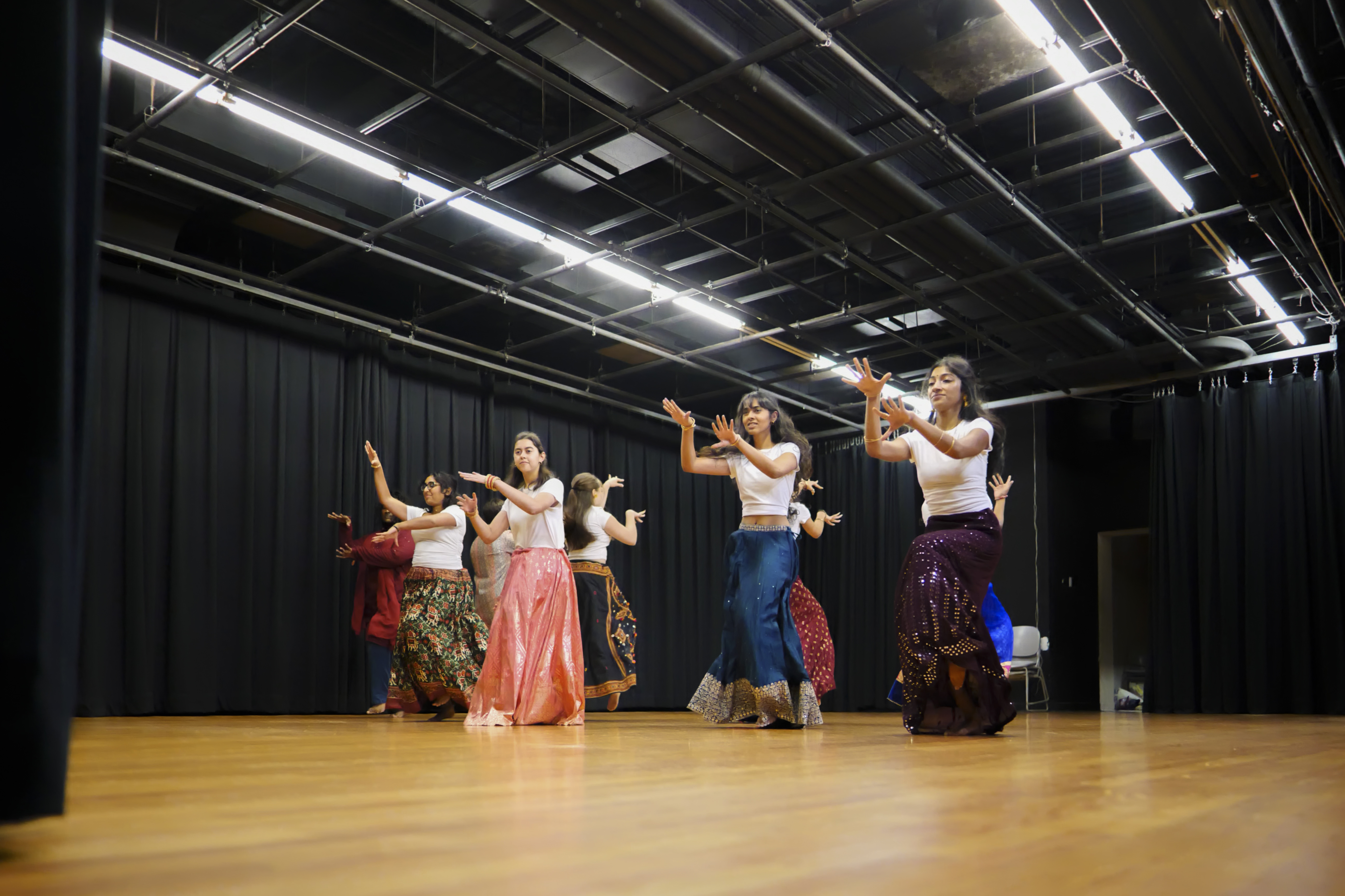 A group of people do a synchronized dance in a room with wooden floors