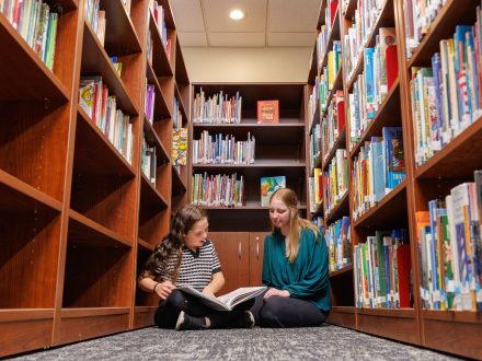 Photo of a child and a college student reading a book together on the campus of Elon University in North Carolina.