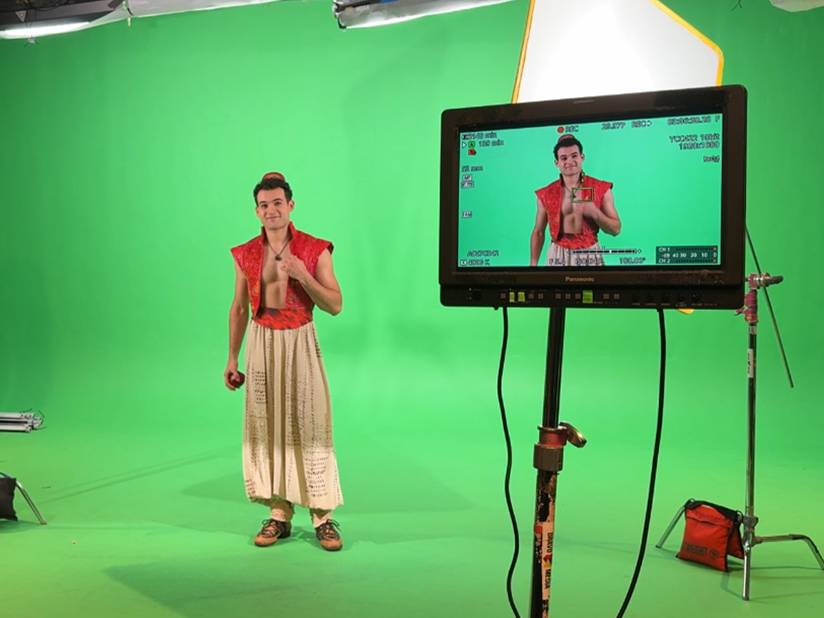 A man dressed as Aladdin stands in front of a green screen