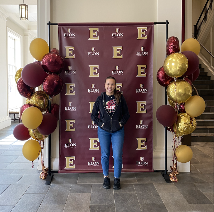Malia Cortes stands in front of an Elon celebration banner and balloons