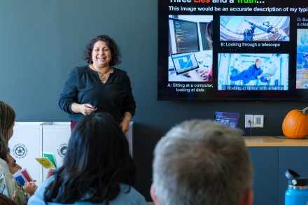 A woman speaks in front of people with a presentation screen