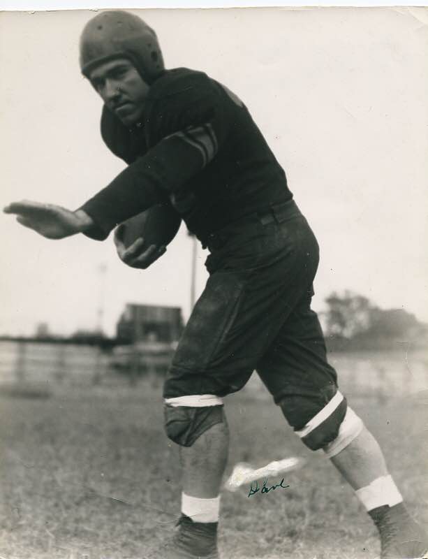 Black and white photo of a man in a football uniform, in an active pose holding a football