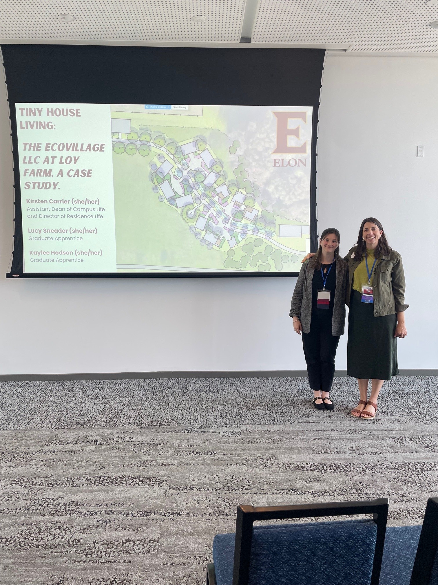 Two women stand next to a presentation screen