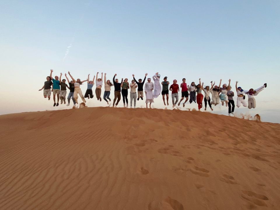 A group of people in a line jump into the air on a sand dune