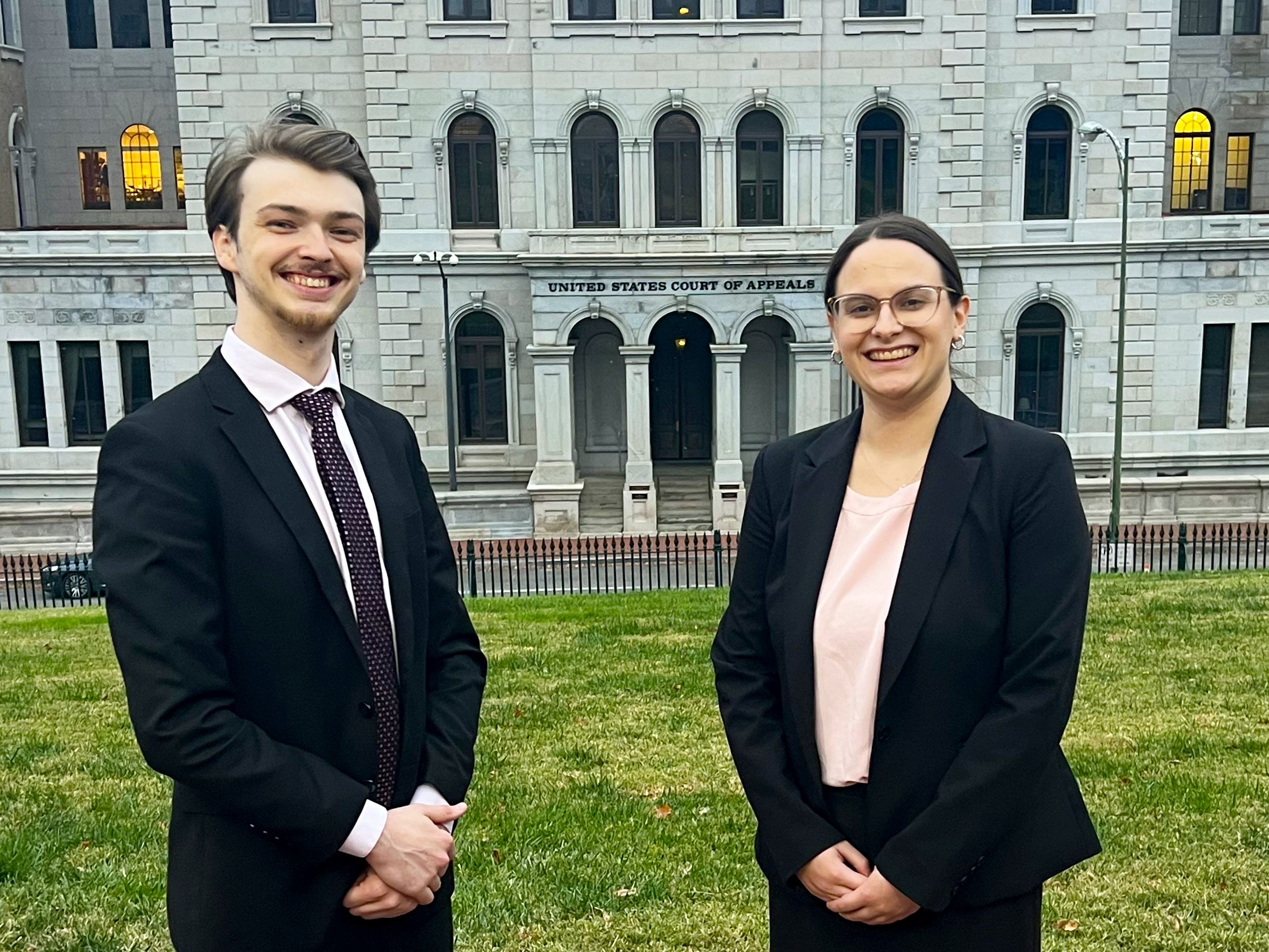 Two students in professional dress in front of a Federal Circuit building.