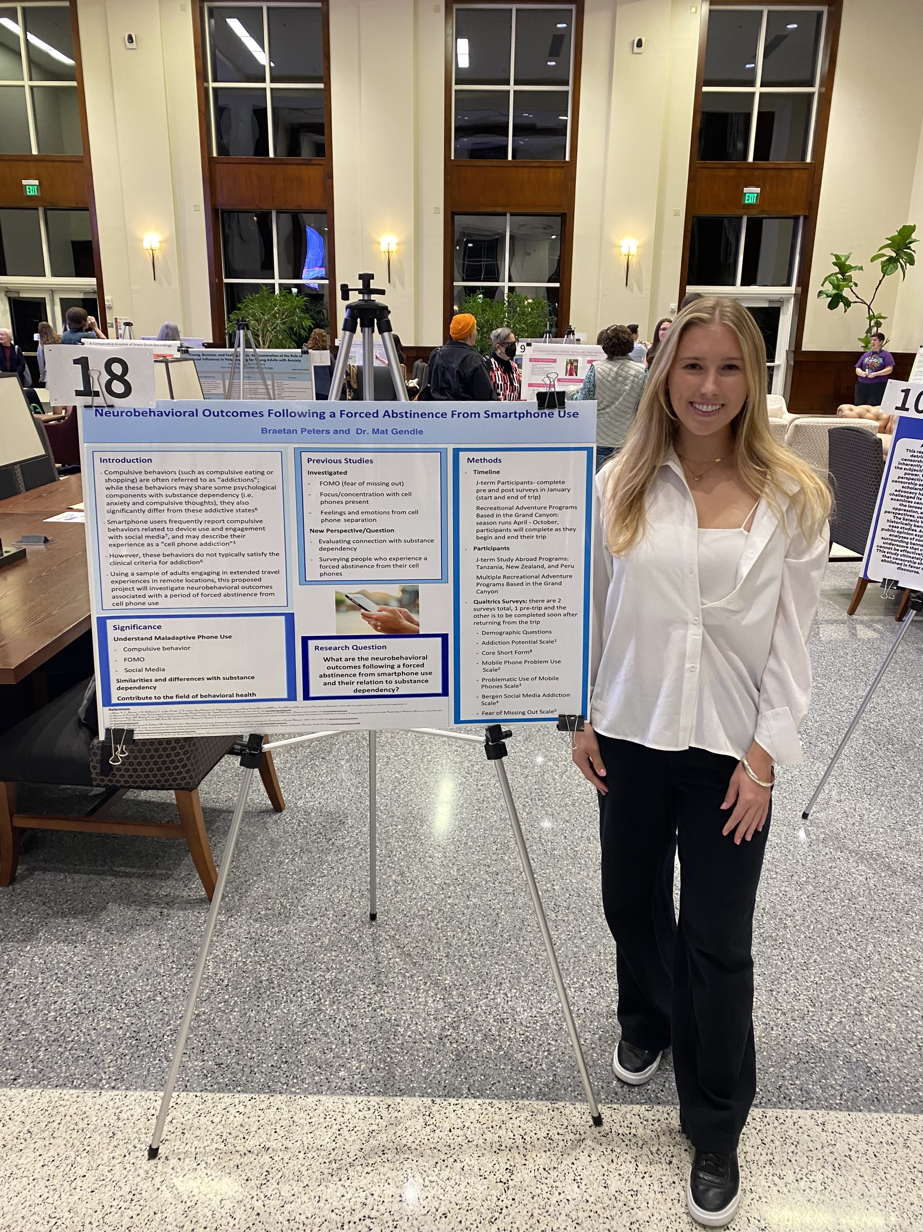 A woman in a white shirt and black pants poses next to a research poster
