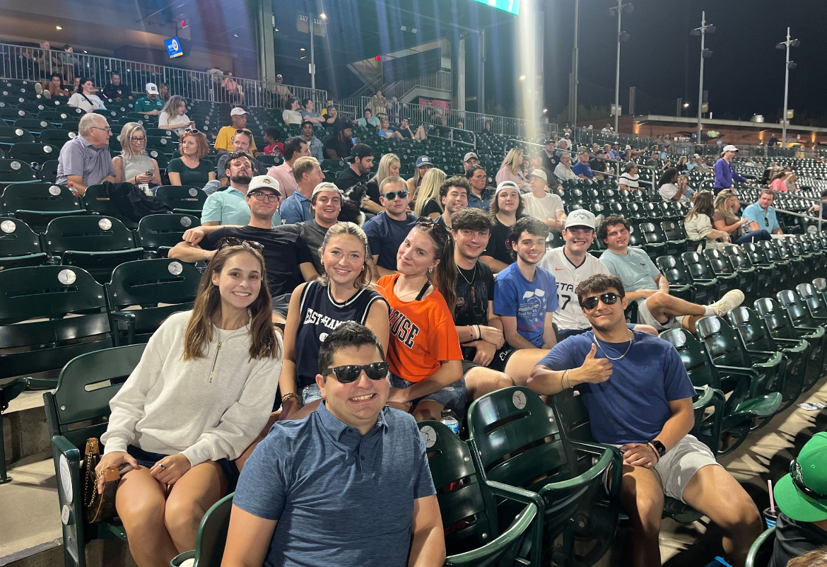 A group of people smile together at a sports game in the stadium stands