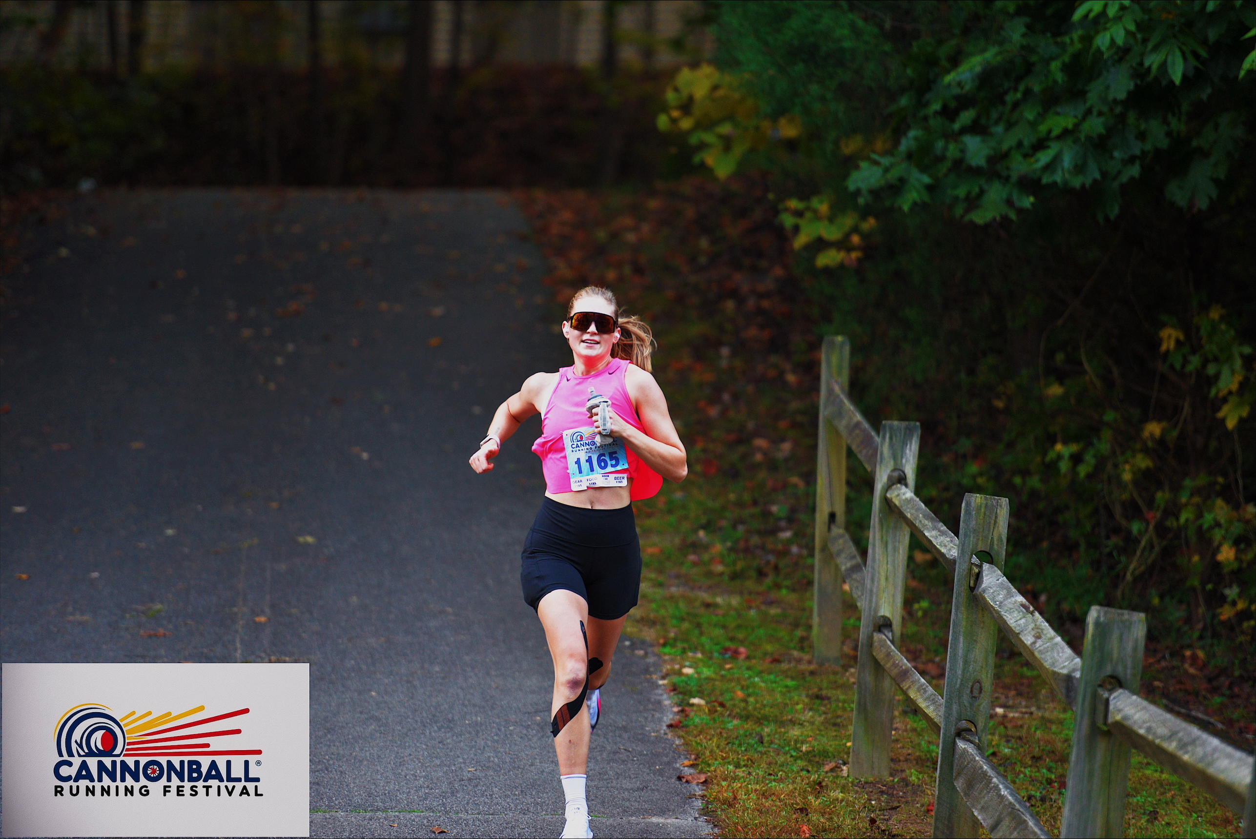 a woman running on a road surrounded by trees and a split-rail fence.