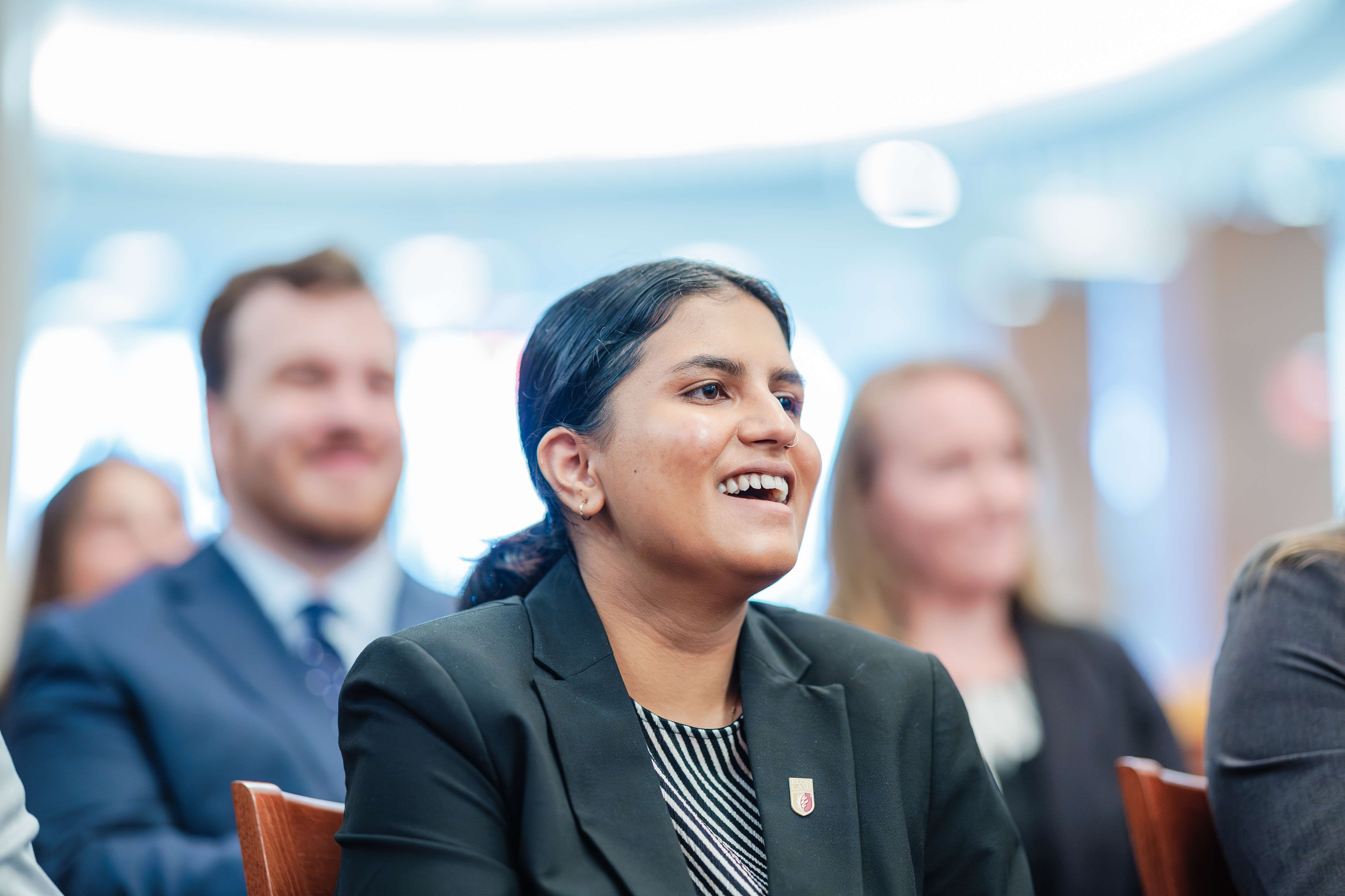 A woman laughing in a seated audience inside a courtroom.