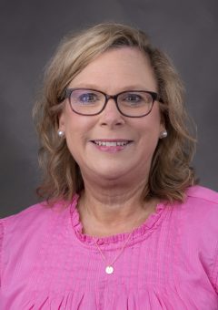 Belinda has medium-length brownish-blond hair and glasses with a pink shirt