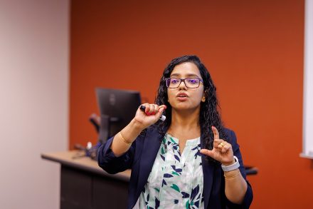 A faculty member gestures while speaking during a presentation in a classroom.