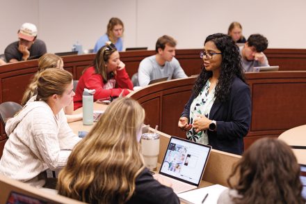 A faculty member speaks with students seated in a tiered classroom during an interactive lesson.