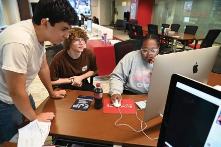 Students work together at desktop computers in a collaborative campus workspace.