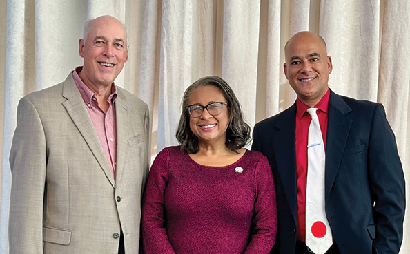 Three university leaders stand together and smile for a formal portrait indoors.
