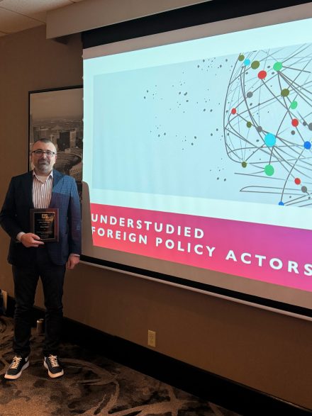Barış Kesgin holding his plaque in front of a screen where he gave a keynote address at the ISA Midwest Conference.