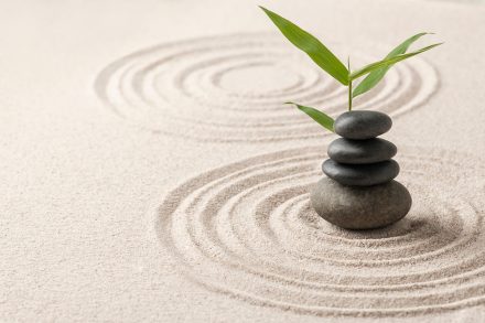 A close up of three stacked stones in a zen garden, positioned in the middle of a series of concentric circles in the sand.
