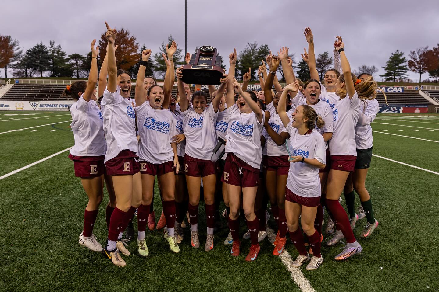 Elon women's soccer team cheers while holding a CAA trophy in the air