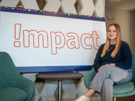 A woman in a blue shirt next to a white board that says "Impact" in orange letters