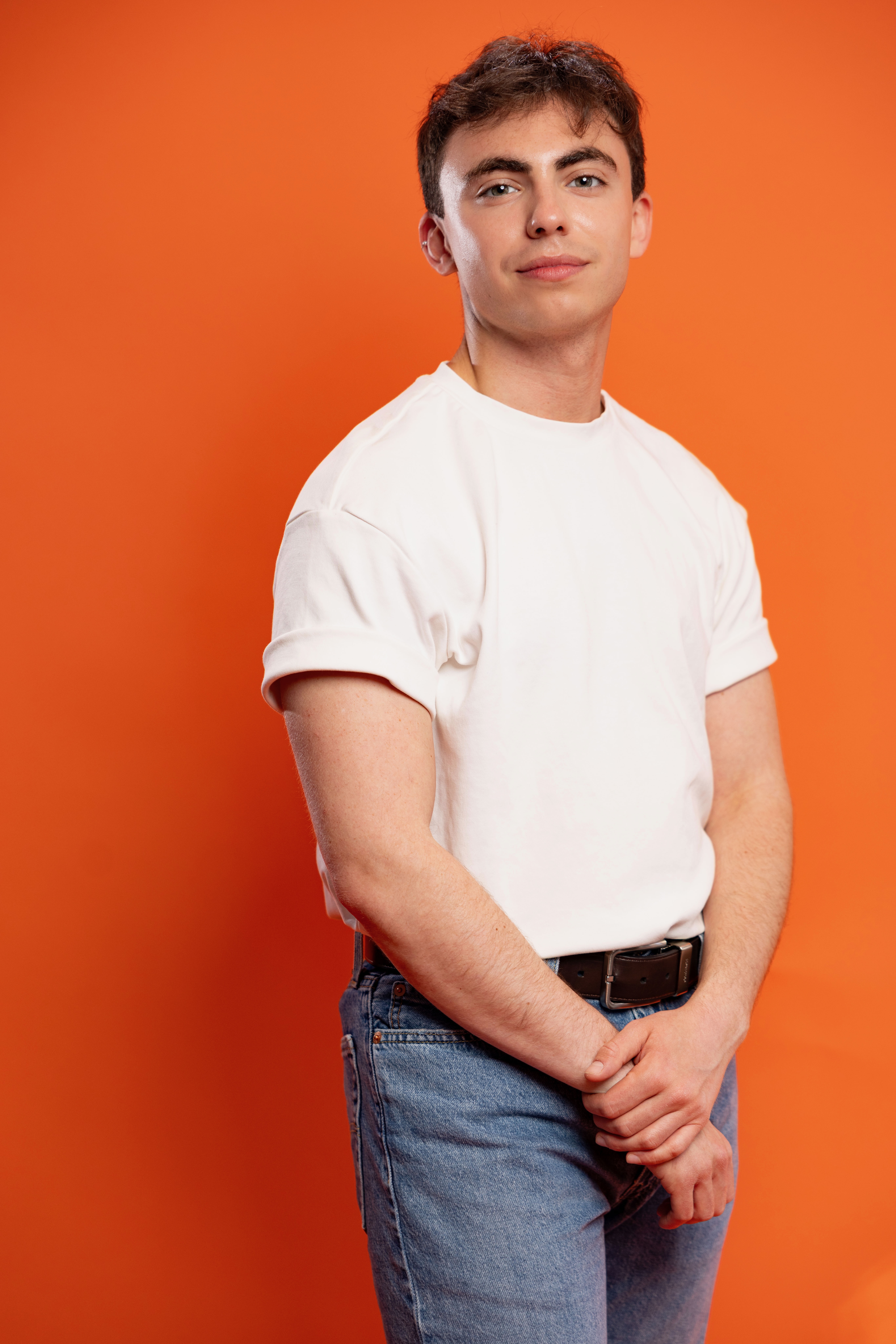 Andrew Stephens Purdy stands in a white shirt and blue jeans in front of an orange background