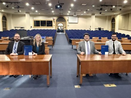Four Elon Law students seated at counsel desks in a large courtroom.