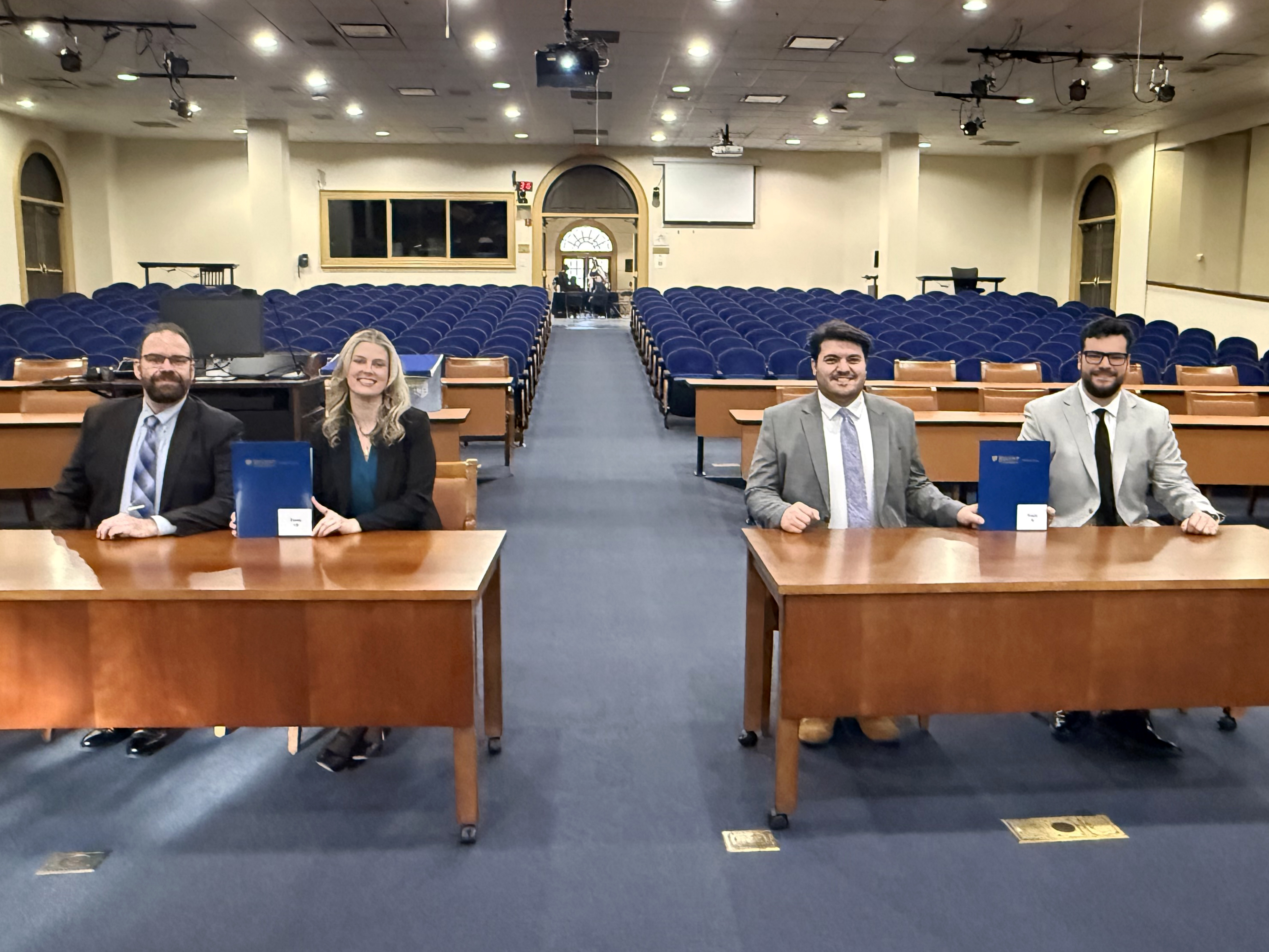 Four Elon Law students seated at counsel desks in a large courtroom.