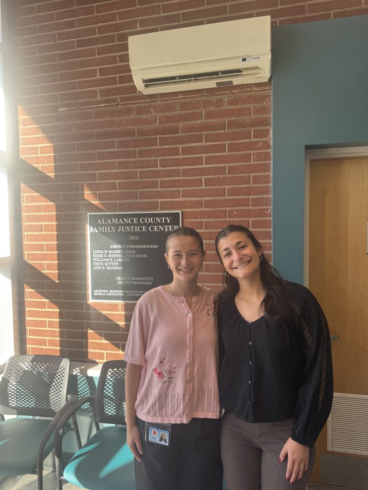 Two female students posing together at their internship at the Family Justice Center of Alamance County.
