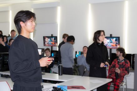 Visiting high school student and a game design student playing a game together. 