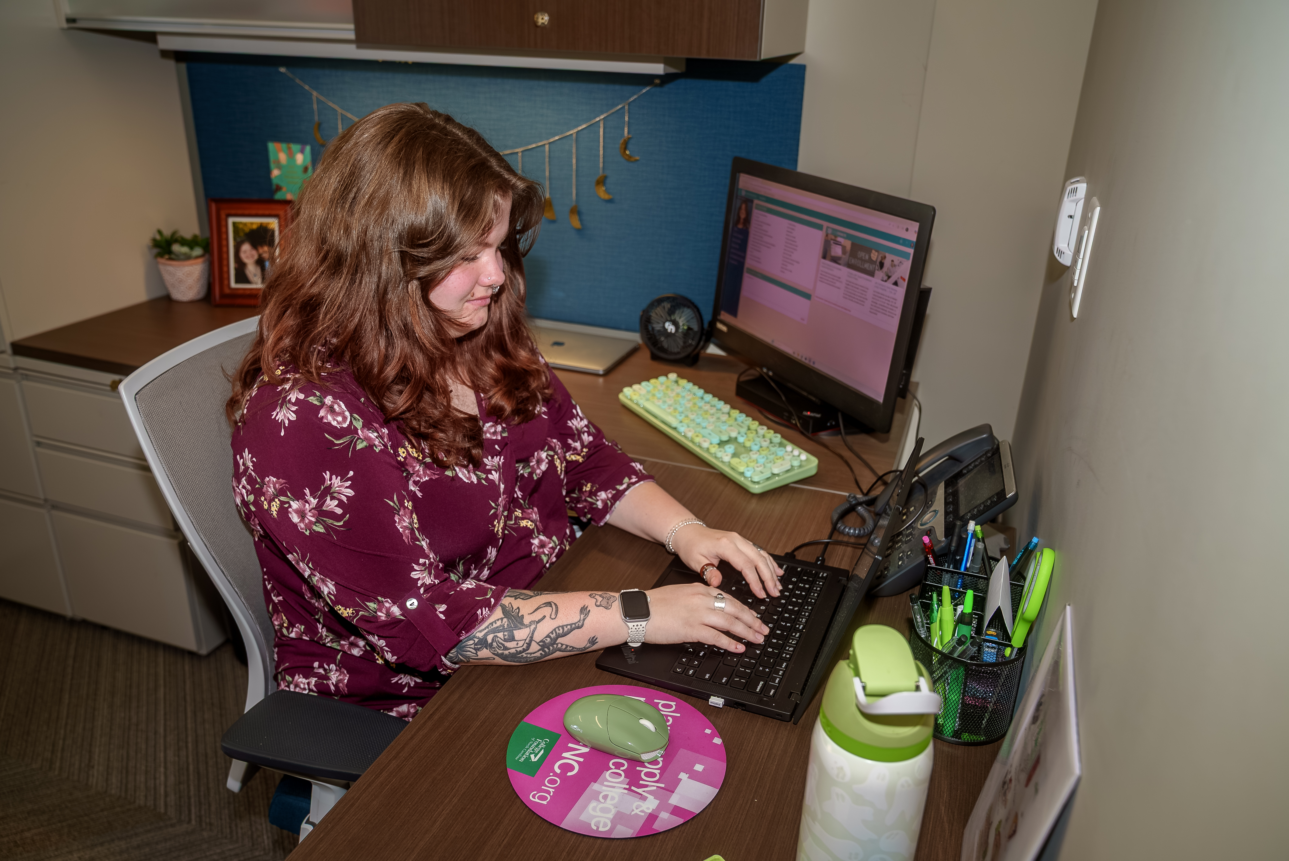 A young woman sits at a desk typing on a laptop