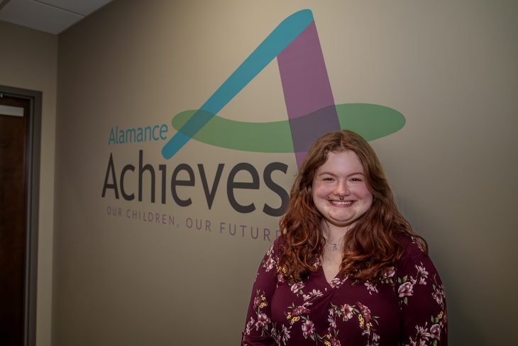 Jasmine Walker standing in front of Alamance Achieves logo