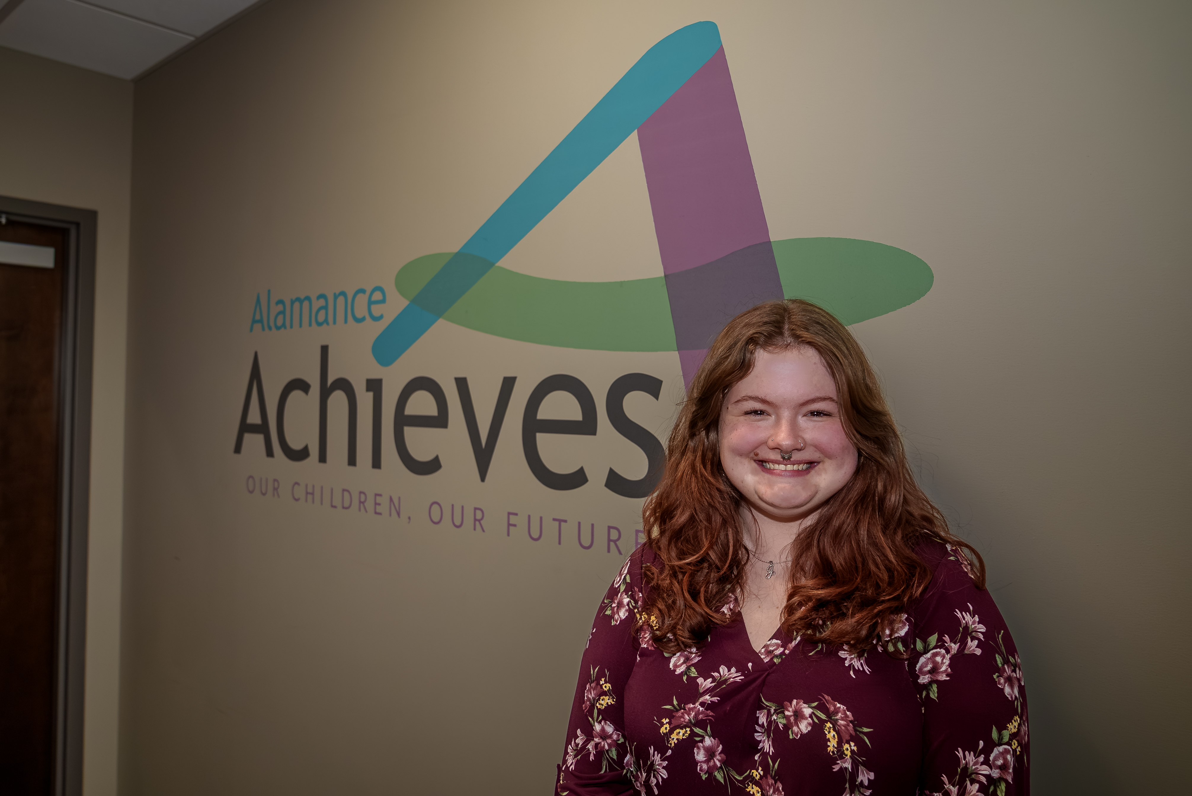 Jasmine Walker standing in front of Alamance Achieves logo
