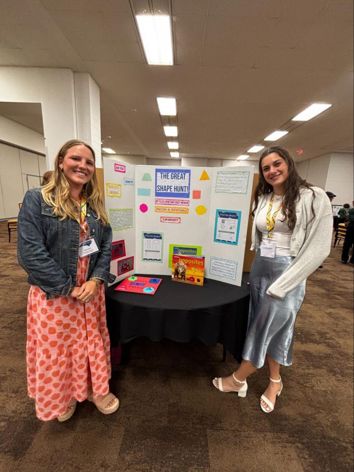 Two presenters stand smiling beside a tri-fold poster titled “The Great Shape Hunt” at an educational poster session. The display features colorful shapes, learning activities, and children’s books focused on early math concepts.
