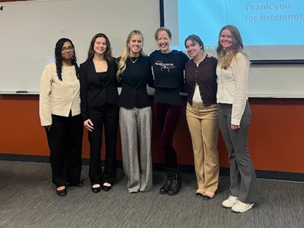 A group of six people pose for a photo in front of a projector screen