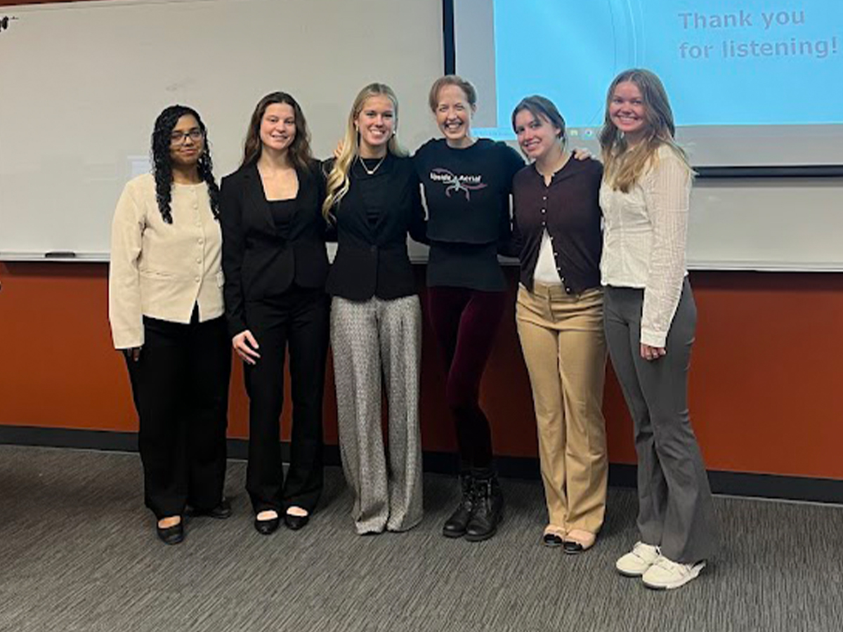 A group of six people pose for a photo in front of a projector screen
